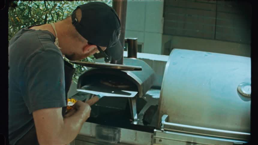 A man inserts a pizza into a backyard oven