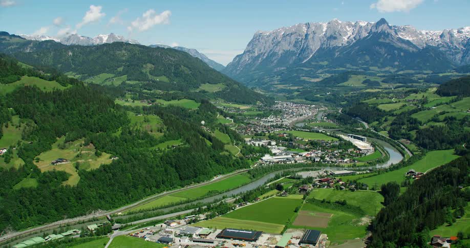 An aerial view of a small rural town with a huge asphalt street and a river running through the green hills vegetation