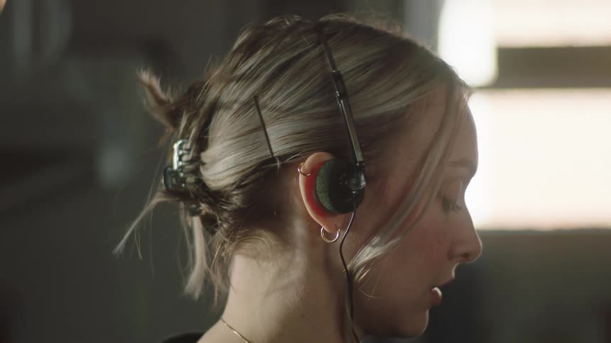 A blonde woman with tied hair is putting headphones in her ears