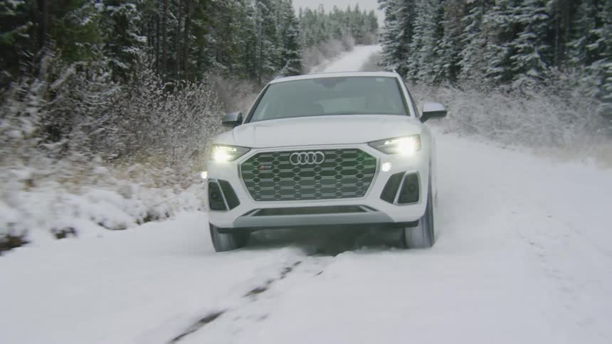 Audi brand vehicle moves along snow covered road passing conifer forests during winter