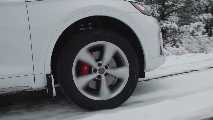 Wheel of a car moving along a road covered in snow and with conifers on the side