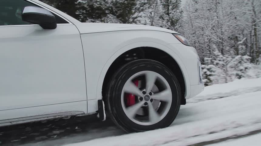 A closeup of the front wheel of a white car driving on a snowcovered road