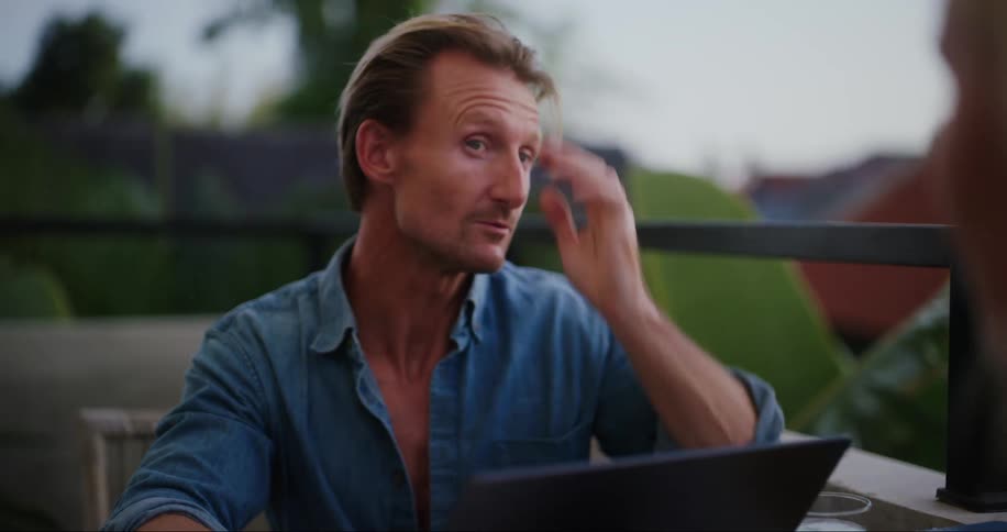 A man sitting at a restaurant table with a woman talking while looking at a laptop