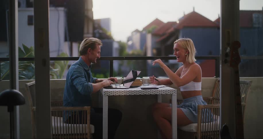 A man and a woman high five one another while sitting at a table on a balcony