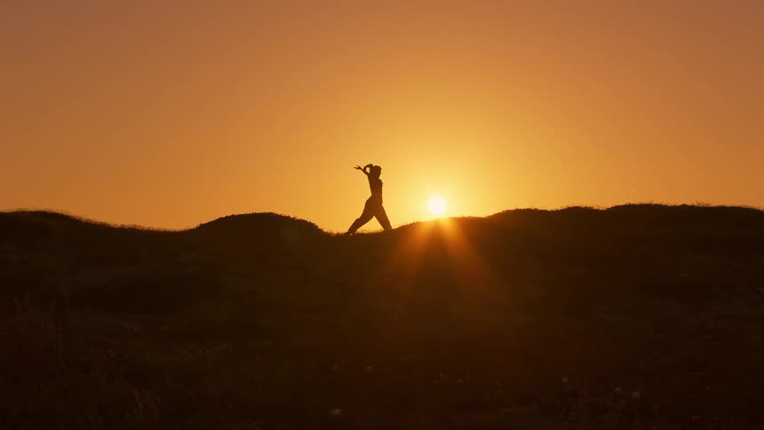 Silhouette of a person on a mountain peak against an orange sun dancing