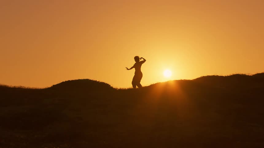 A silhouette of a person doing yoga exercises with their arms against a very orange sky