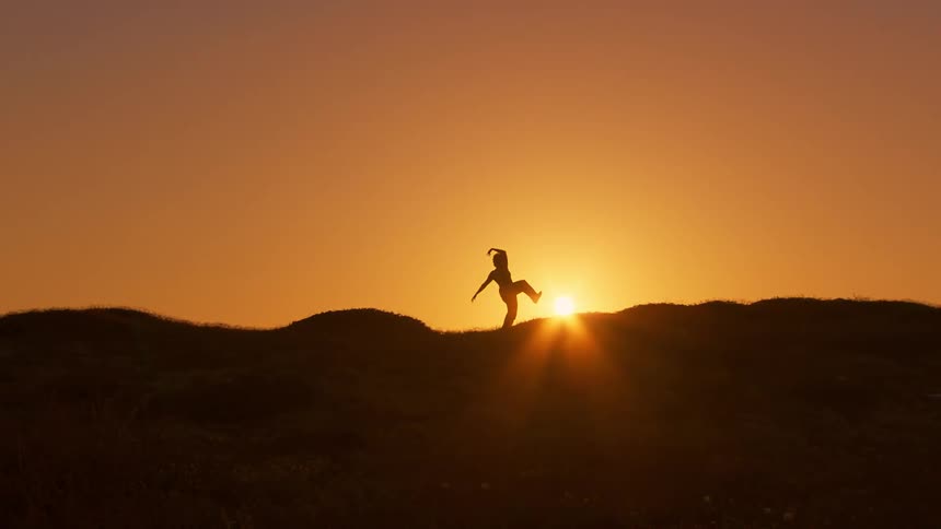 Dancer in silhouette on hillside at sunrise