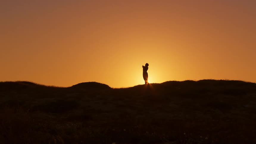 A woman backlit by the sun does stretches outdoors