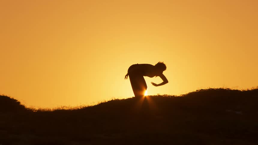 A person dances on a hill at sunset
