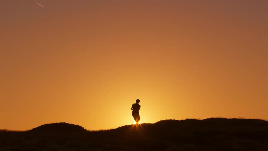 A silhouette of a woman dancing over a hill against the backdrop of a setting sun