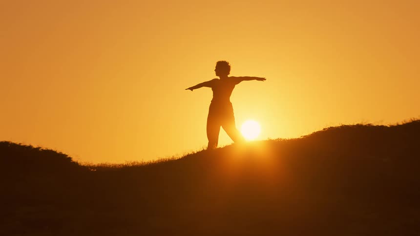 A woman is practicing tai chi at sunrise