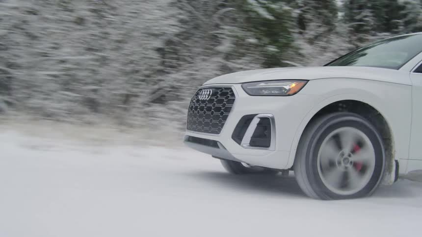 A white vehicle drives on a snowy road near a forest