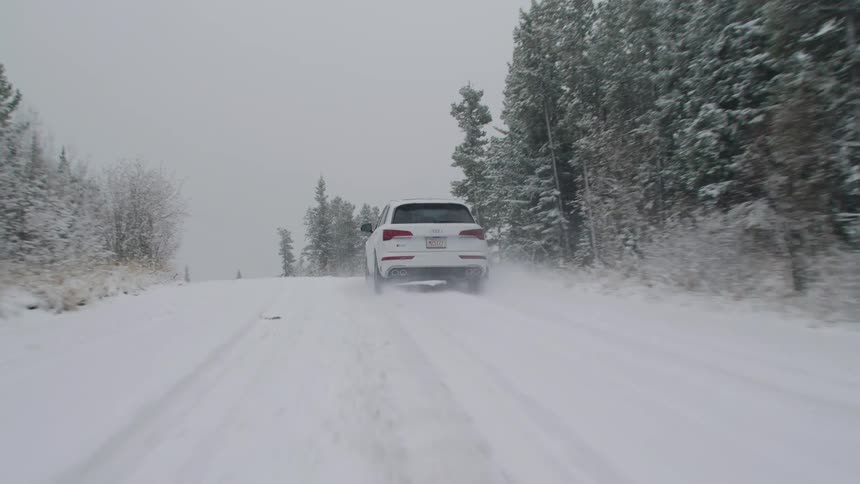 White audi suv traveling down a snowcovered road with conifers around