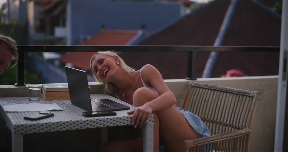A young couple seated at a table laughing together in an outdoors setting at dusk