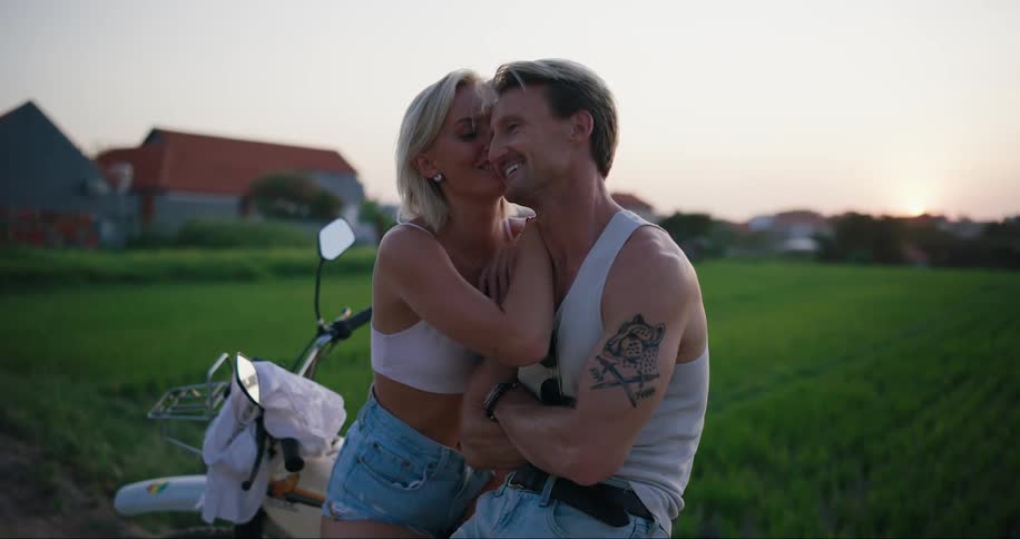 A woman kisses a man while standing near an agricultural field