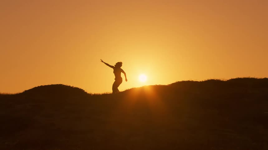 Dancer in silhouette on hillside at sunrise