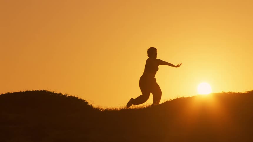 A woman is stretching on the hill at sunrise