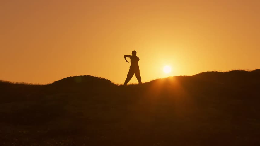 A silhouette of a person making martial gestures against an orange sky of a bright bright sun