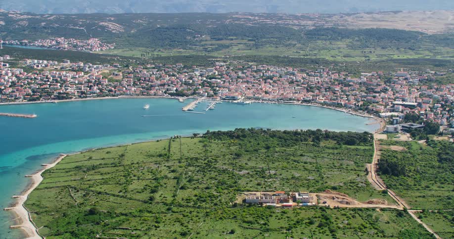 A large coastal city with many houses facing the crystal clear sea water and a huge grass field with just one building in front