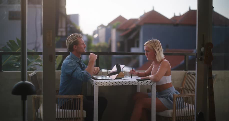 A man and woman sit together on a balcony while having a discussion
