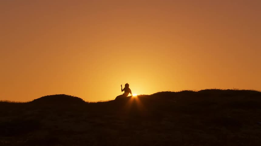 Dancer on hillside in silhouette at sunset