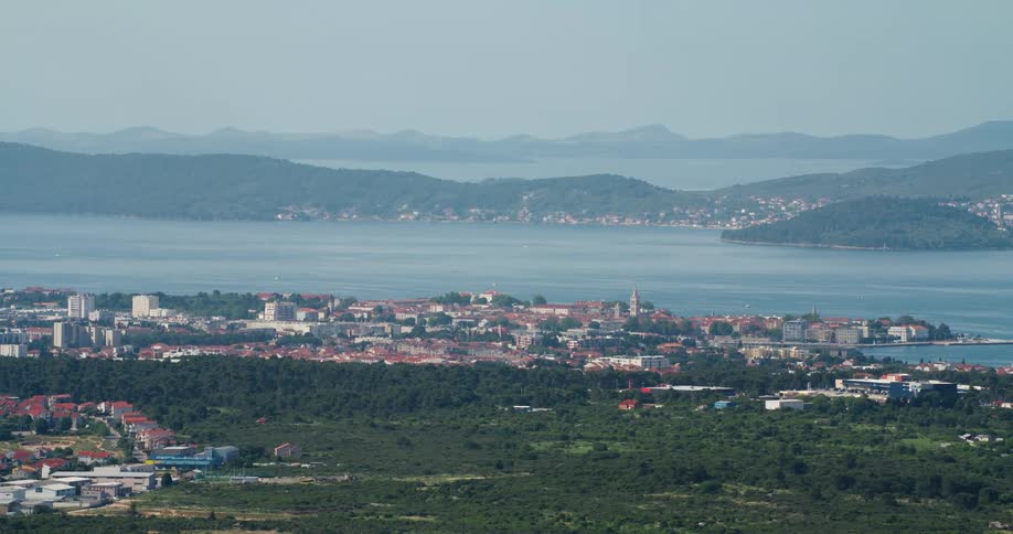 An aerial view of a city facing a bay of water with an island full of trees in the middle