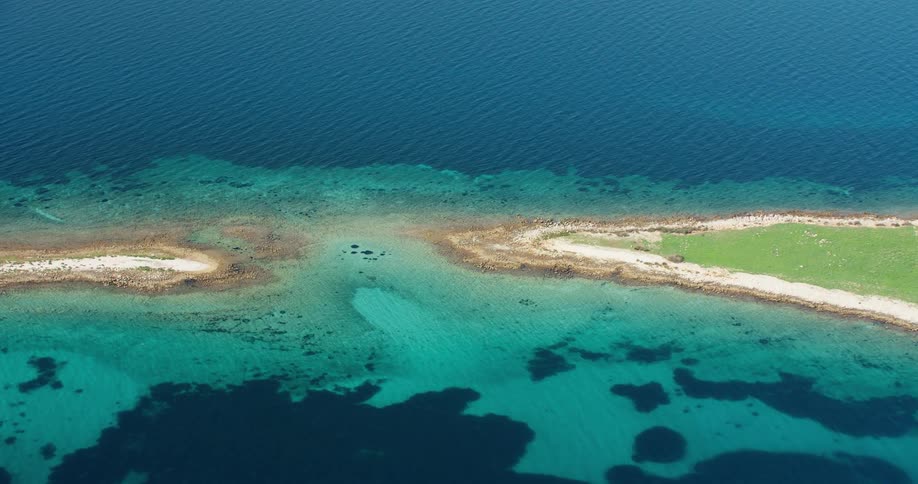 An aerial view of two islands divided by crystal clear water and green grass on the surface