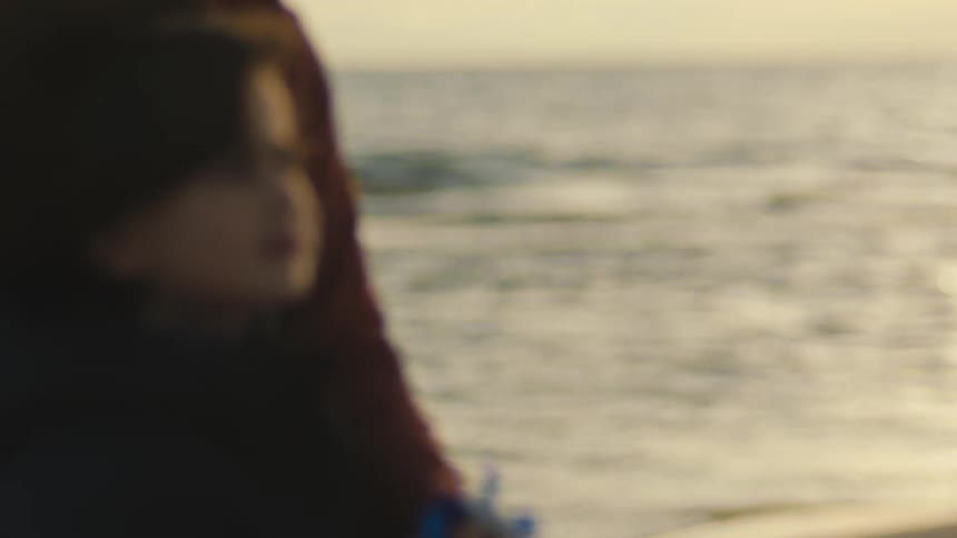 A boy flying a kite on a beach with an adult by his side