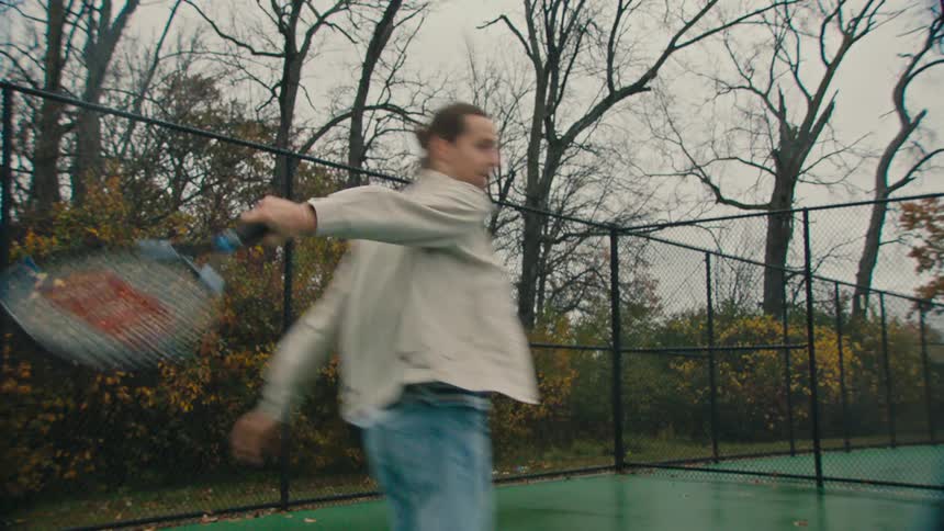 Man playing tennis on an openair court with trees in the background