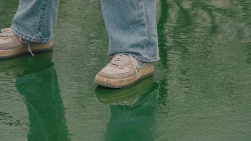 Person wearing jeans stands on wet reflective pavement