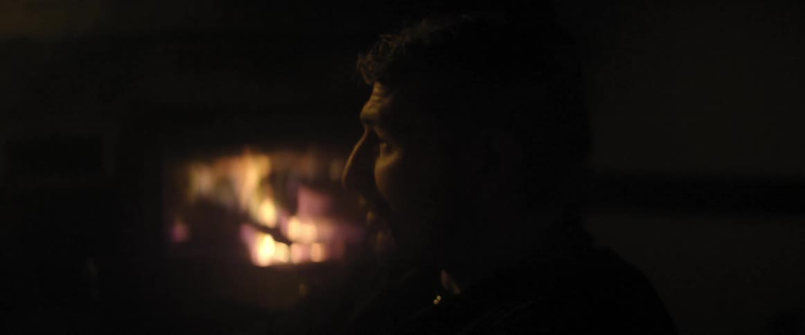 Man smoking in a dark area with fire behind him