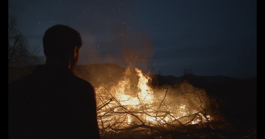 A man watches a fire at night