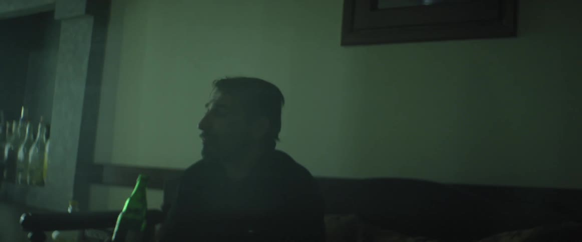 A man drinks from a bottle in a dark room