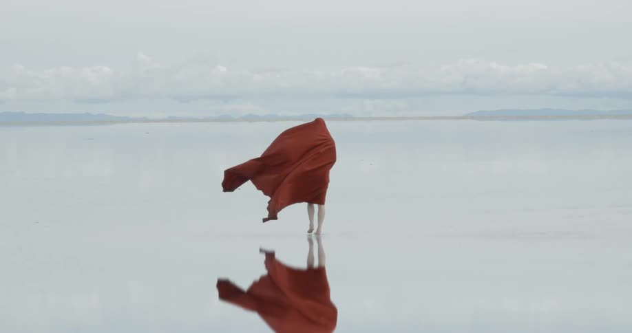 A person is walking along a reflective field wearing red robes