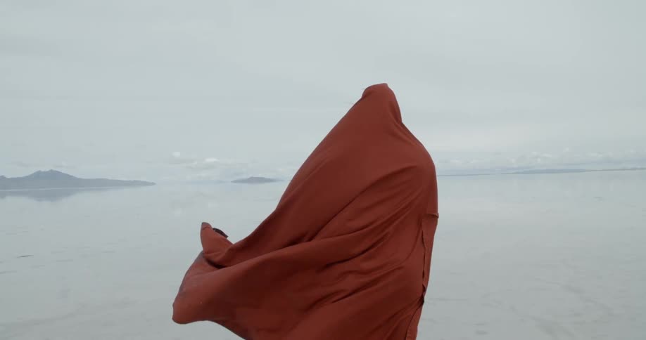 A large piece of material being worn by a person is blowing in the wind