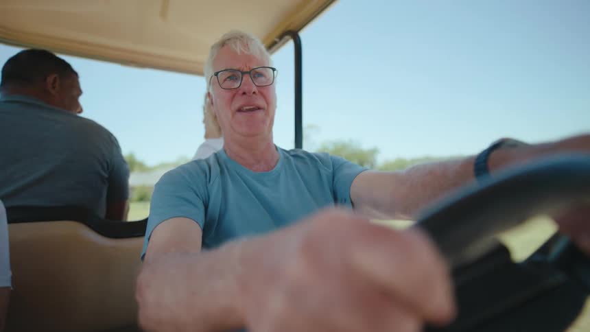 The face of an elderly man who is talking while driving a golf cart