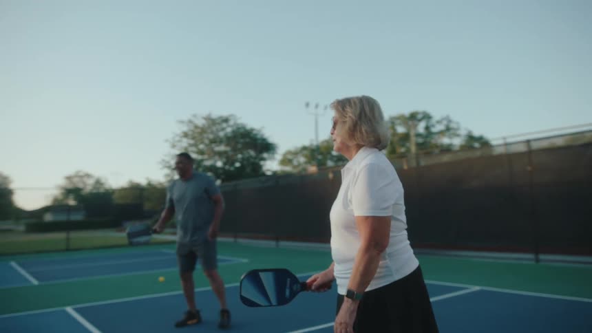 An elderly couple practice hitting pickleballs across the net
