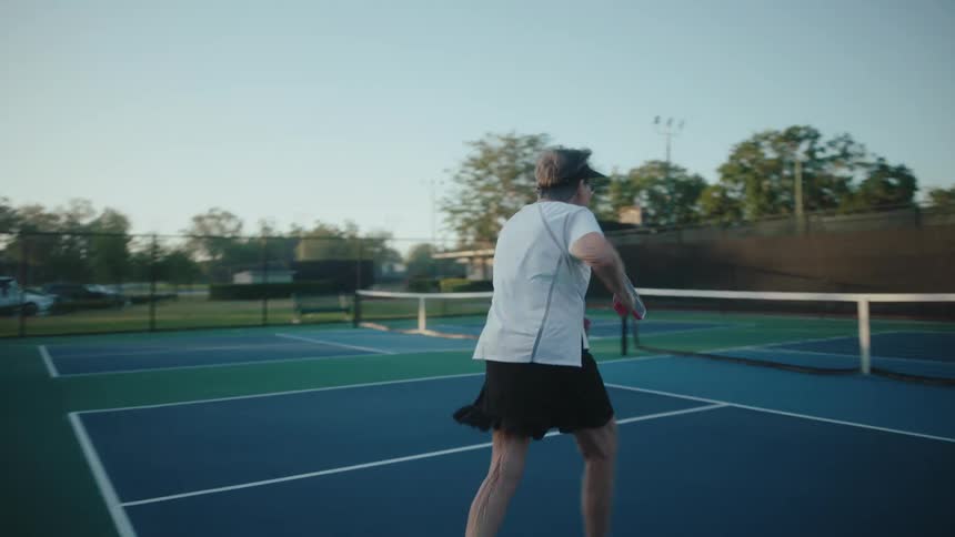 An elderly woman trying to hit a pickleball during a game