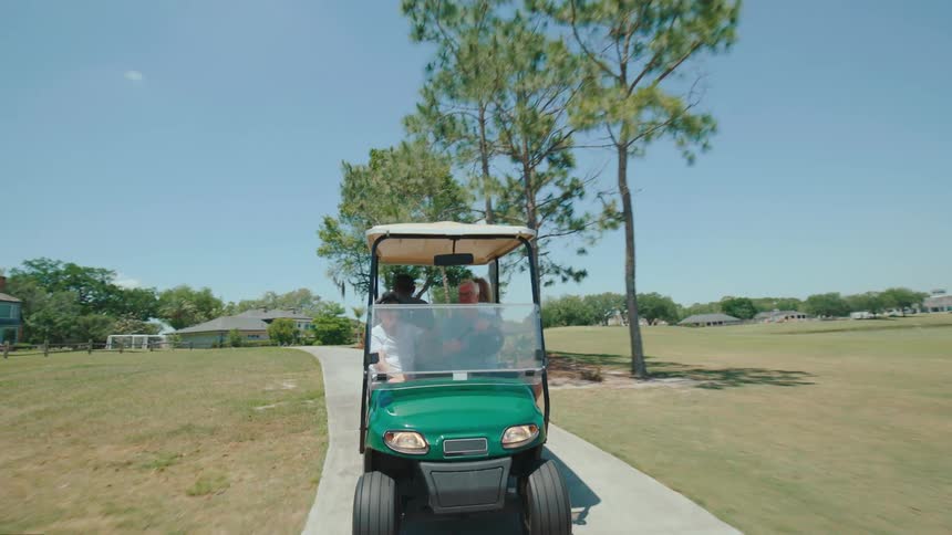 A small green golf cart being driven by an elderly man on a concrete path and surrounding grass