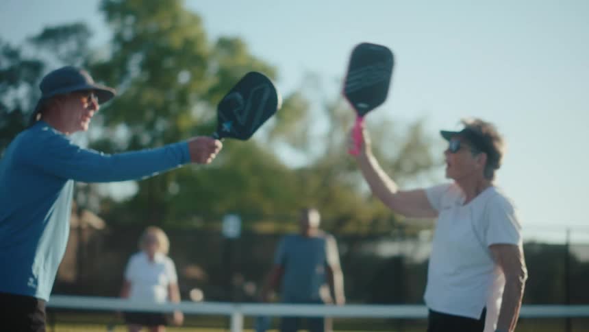 Two pickleball players tap paddles while playing a pairs game