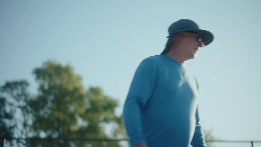 Man in blue shirt and hat playing pickleball