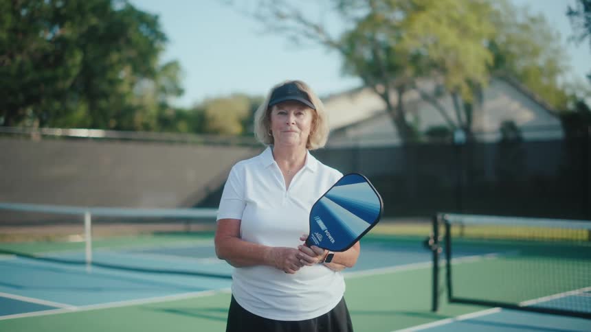 Elderly woman on a tennis court holding a pickleball paddle