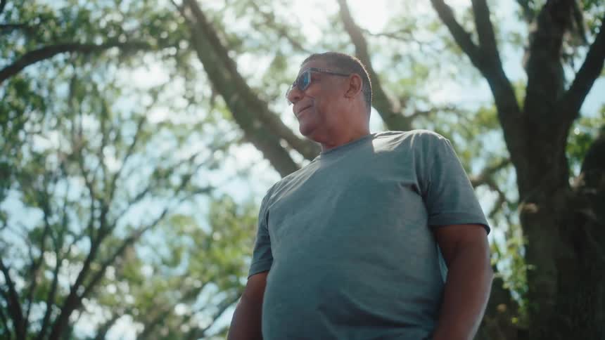 A man wearing sunglasses talks while standing near a grove of trees