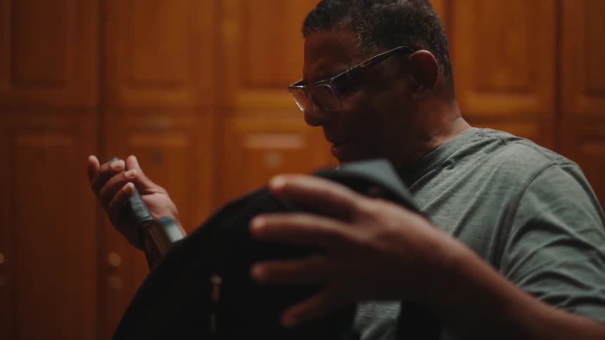 An ethnically diverse man in a mens locker room adjusting sports equipment in his backpack