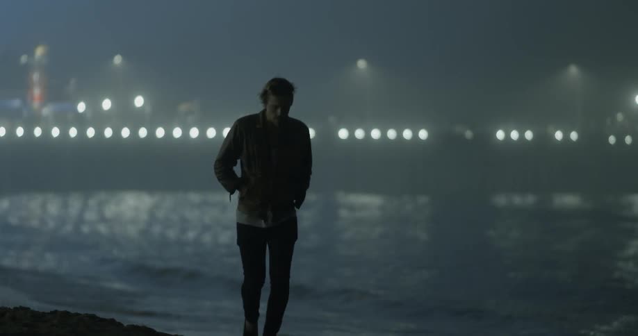 A man walks along a beach at night time