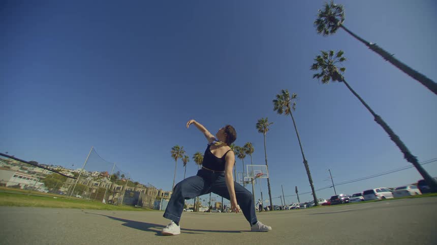 A young woman doing dance moves outdoors with a clear blue sky