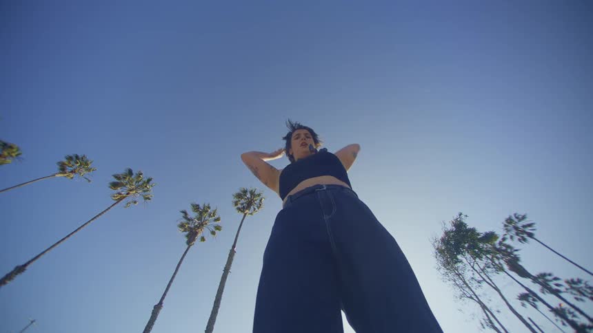 Woman dances outside near palm trees on a sunny day