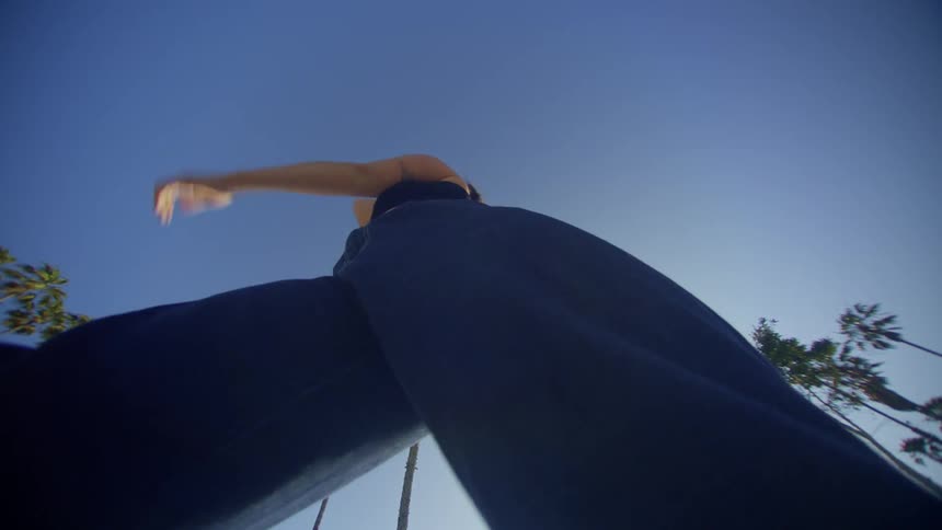 Upward view of a woman in jeans dancing against a blue sky