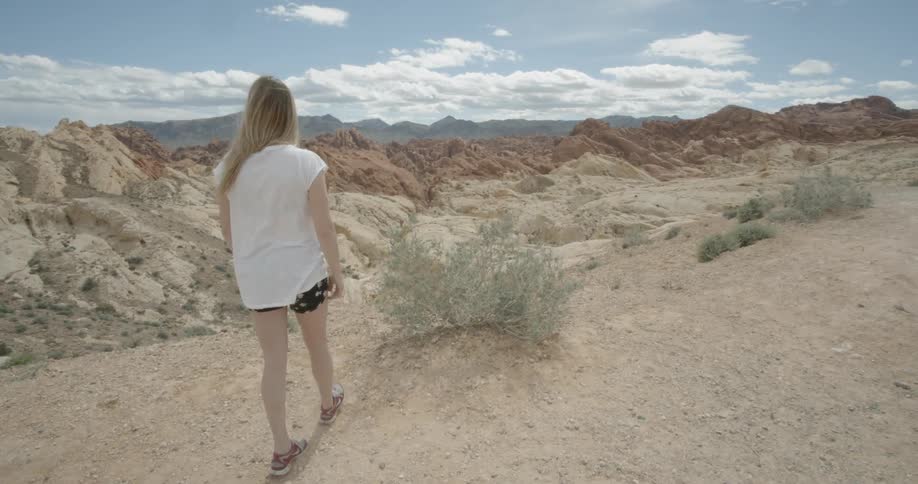 A girl is walking toward the edge of a canyon on a sunny day