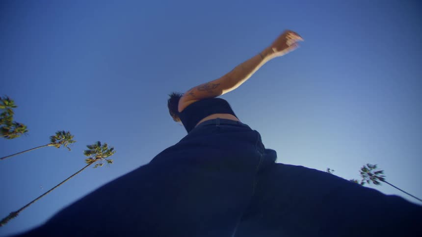 Upward view of a woman dancing against a blue sky